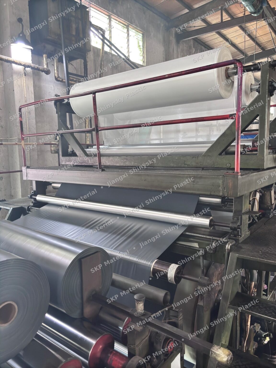 PVC lamination line at the Jiangxi plant: white film feeding from the upper roll and grey coated sheet running out over chrome rollers