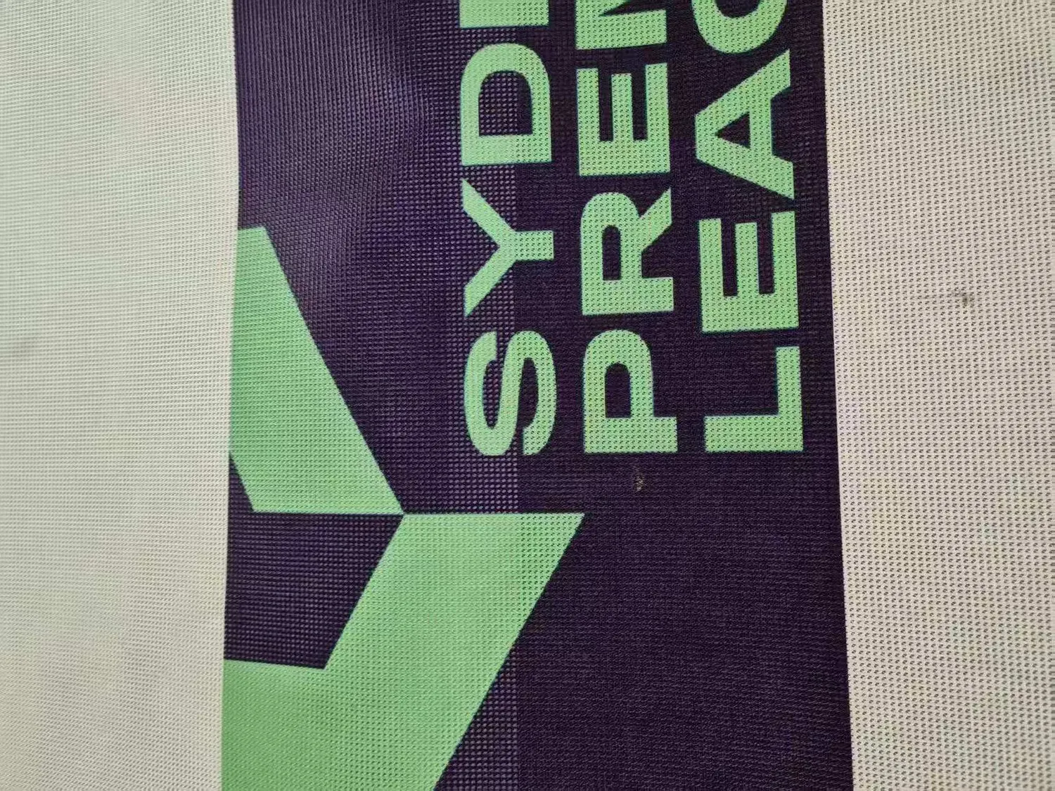 Close-up of a printed soccer mesh banner showing full-colour artwork across the perforated surface