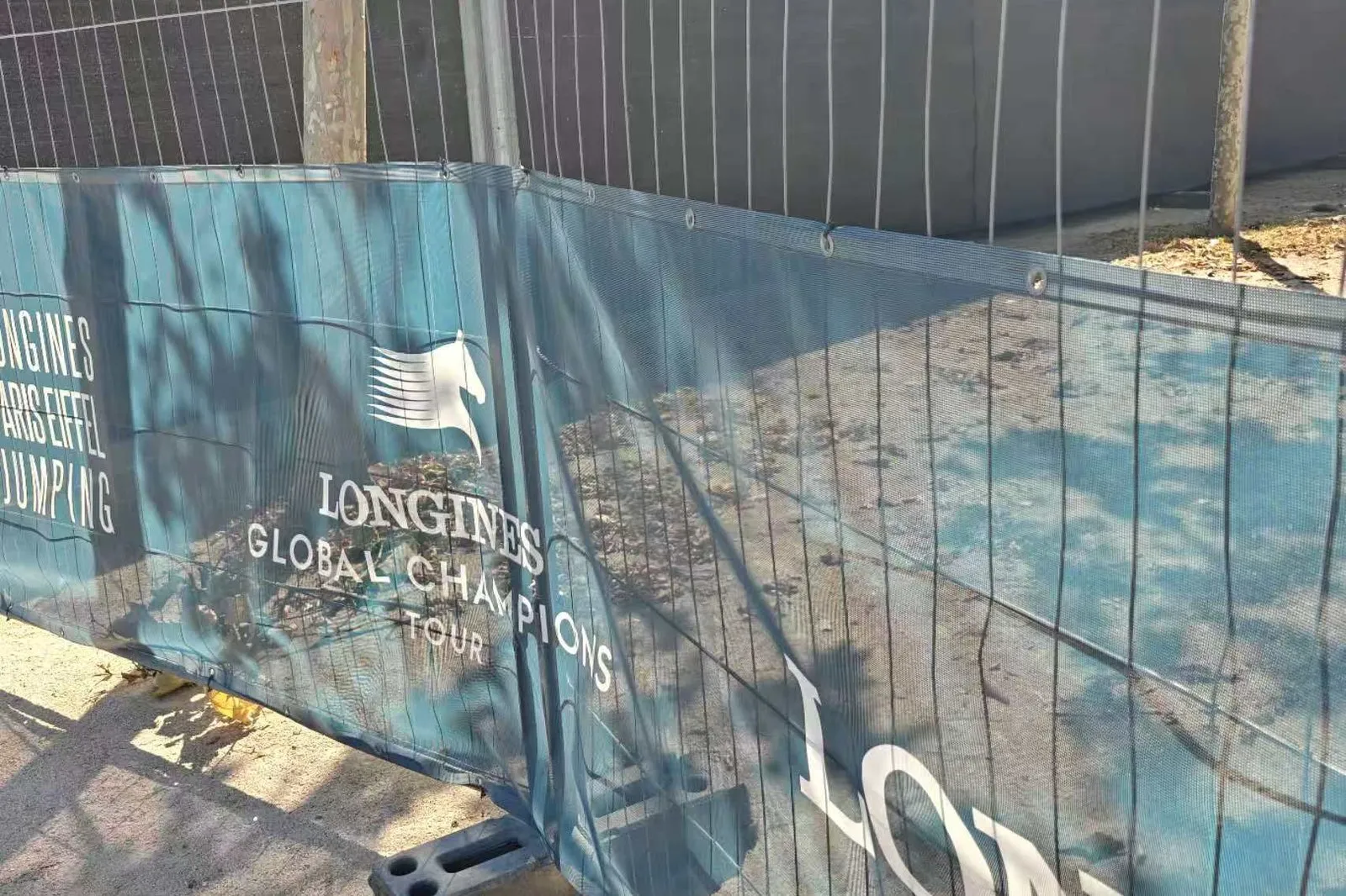 Printed PVC mesh banner fixed through its top eyelets to temporary fence panels at an outdoor event
